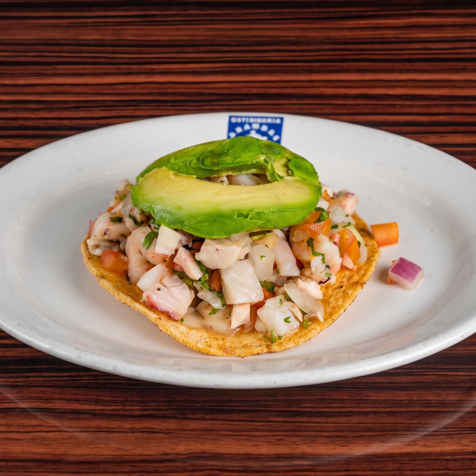 Ceviche tostada with diced fish, shrimp, tomatoes, cilantro, and avocado on a white plate.